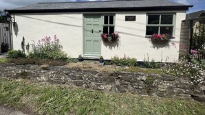 Une charmante petite maison avec une porte verte, deux fenêtres ornées de jardinières et une enseigne indiquant « Palmer’s Lodge ».