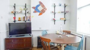 A dining area with a round table, chairs, a TV, and shelves with various items. - Tidewood (Wadebridge)