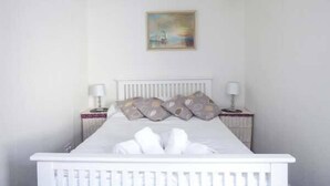 A neatly made bed with white linens and pillows, a white headboard, and a painting above it. - Tidewood (Wadebridge)