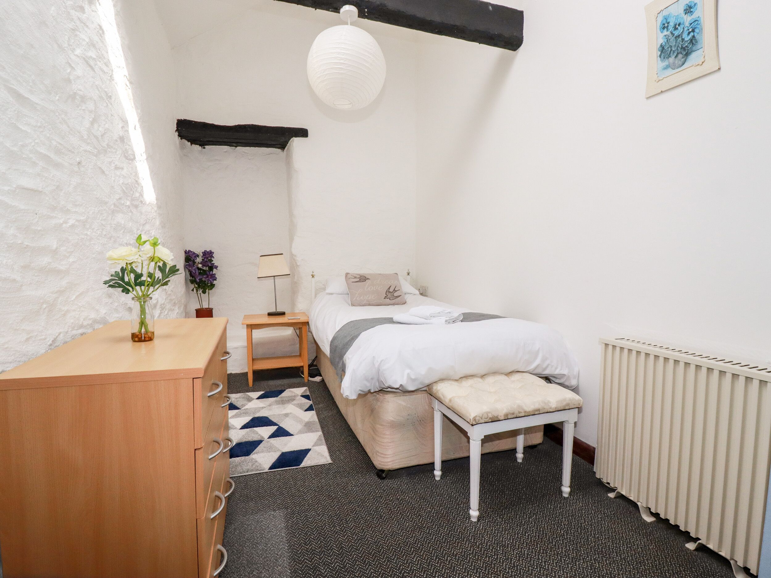 Ein Schlafzimmer mit einem Bett, einem Nachttisch, einer Lampe und einem kleinen Hocker.