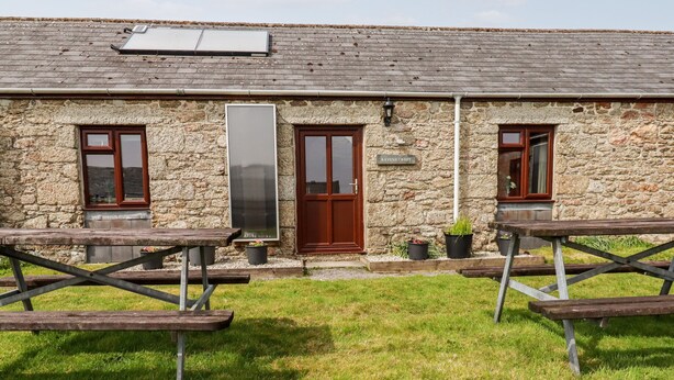 A stone building with a wooden door and windows, a sign reading "Ravens Croft," and picnic tables in the foreground. - Ravens Croft (Bodmin)