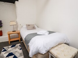 Un dormitorio pequeño y ordenado con una cama individual, una mesita de noche, una lámpara y un pequeño banco.