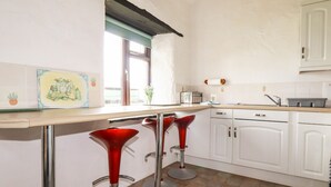 A kitchen with white cabinets, a wooden countertop, a window, and two red bar stools. - Ravens Croft (Bodmin)