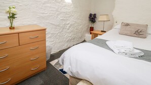 A bedroom with a wooden dresser, a bed with white linens, a lamp, and a pillow with a bird design. - Ravens Croft (Bodmin)