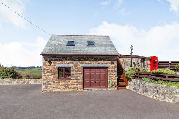 A stone building with a brown door and windows, a staircase, and a red telephone booth. - The Litte Hideaway (Newquay)