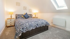 A bedroom with a bed, two bedside tables with lamps, a radiator, and a skylight. - The Litte Hideaway (Newquay)