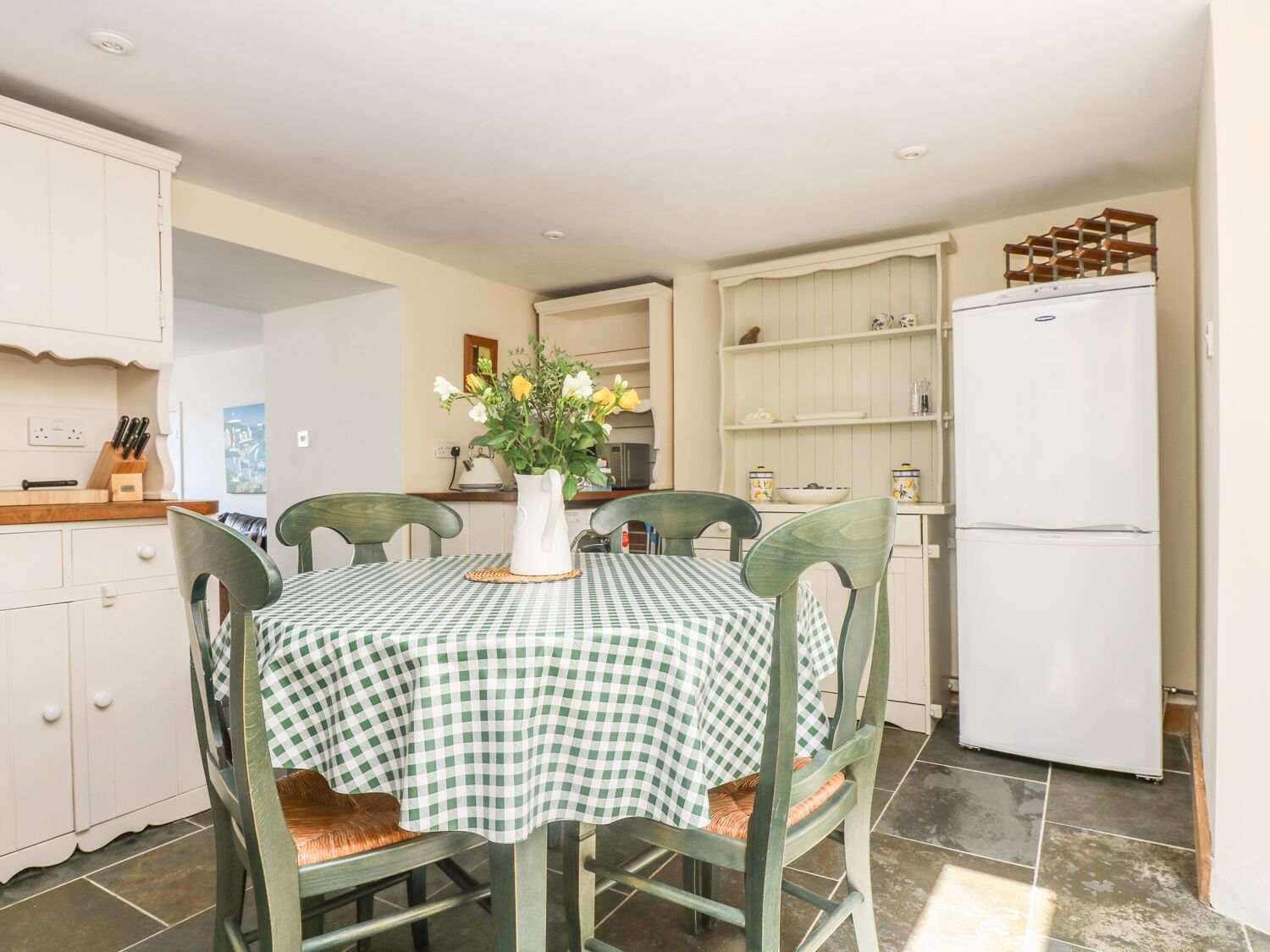 Une cuisine avec une nappe à carreaux, un réfrigérateur blanc et des chaises en bois.