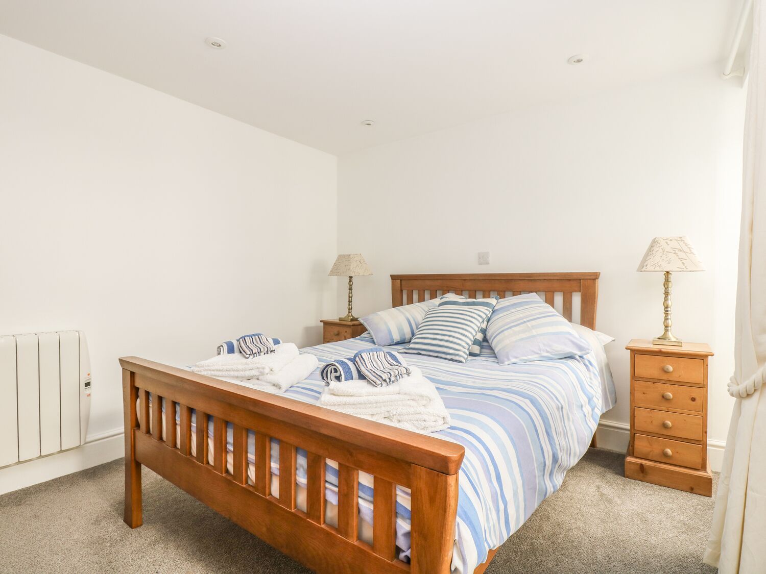 A neatly made bed with striped bedding, a wooden headboard, and two bedside tables with lamps.
