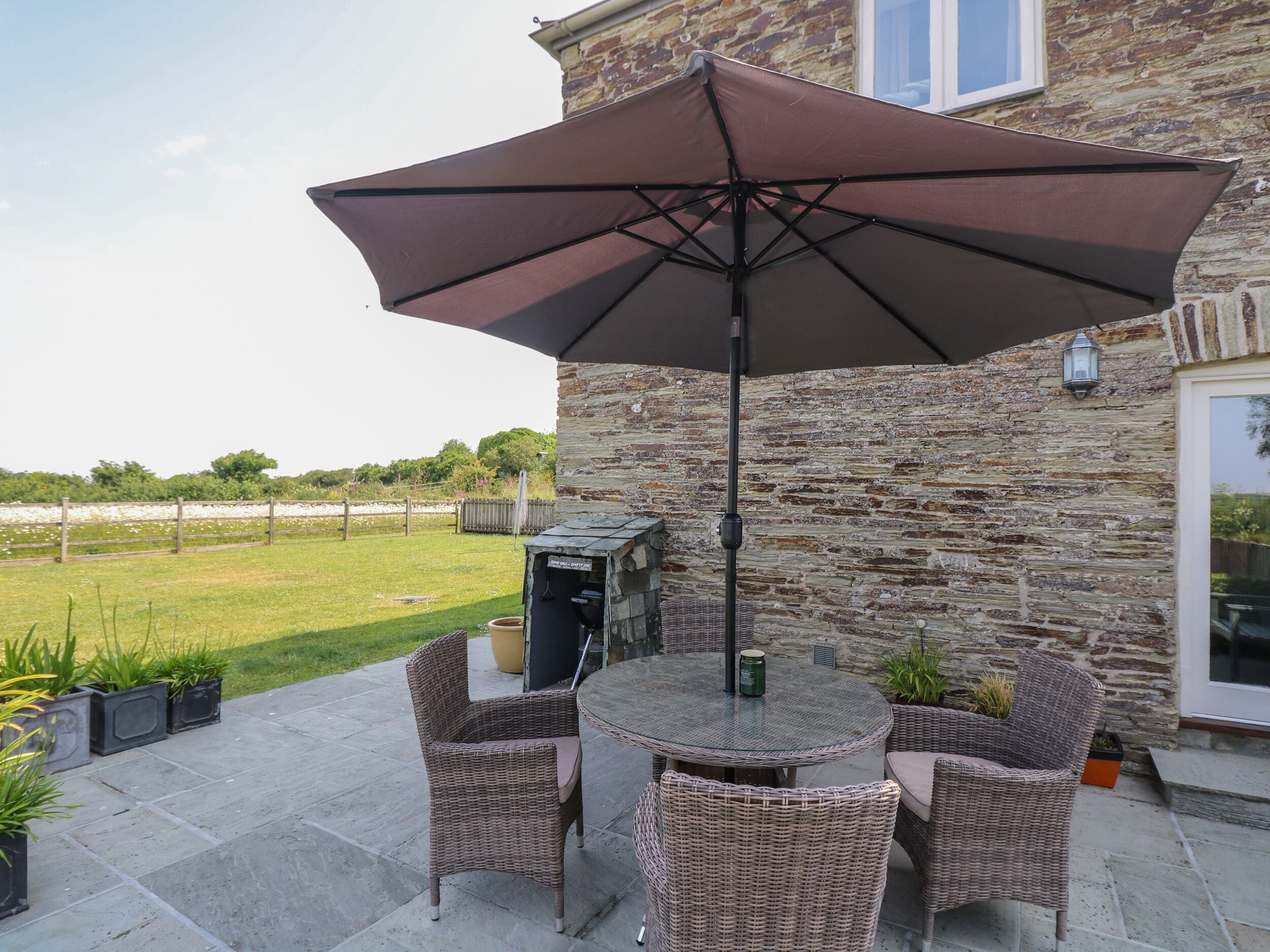 A patio with wicker chairs and a table, a stone wall, and a large umbrella.