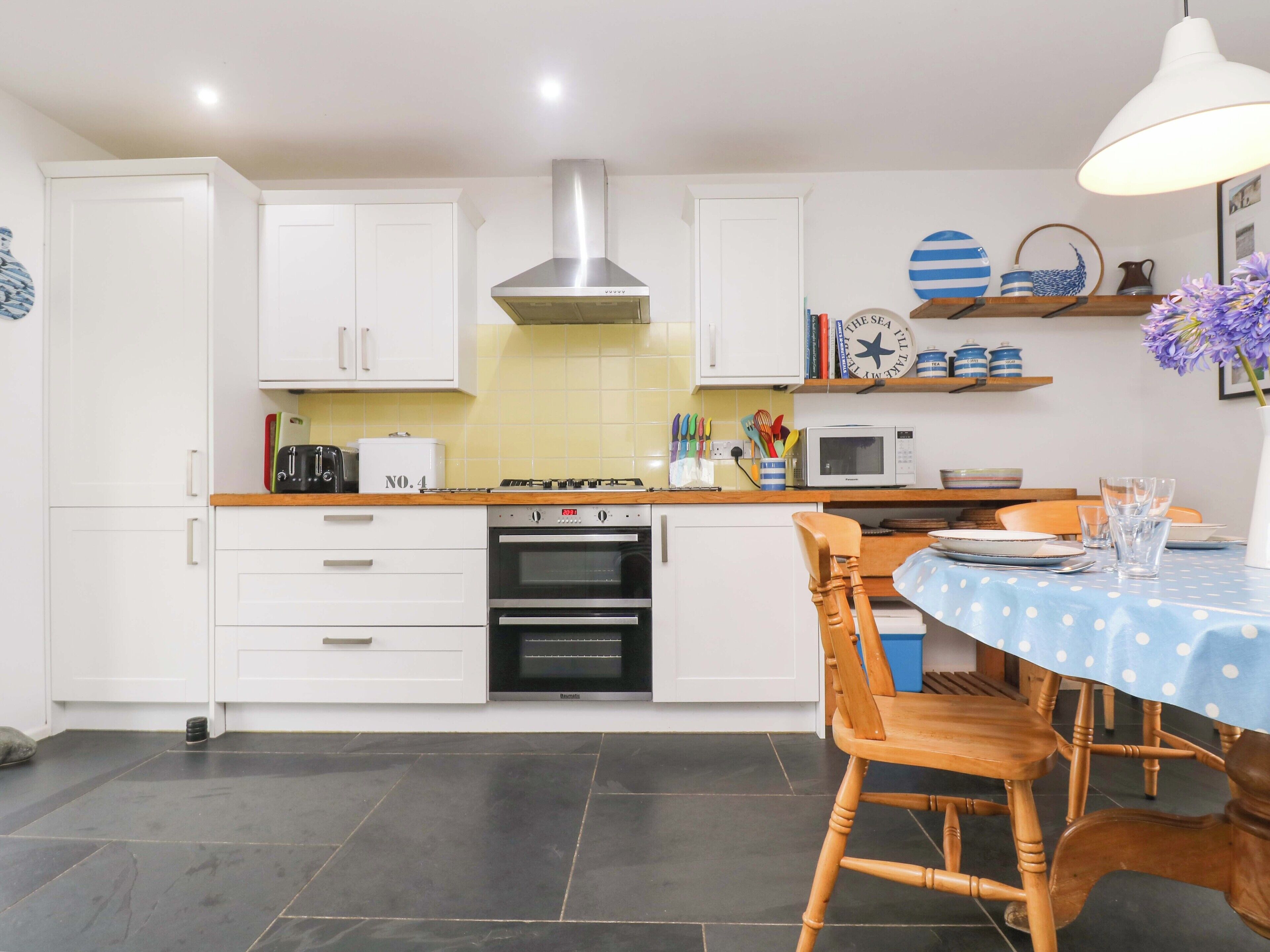 Una cocina moderna con armarios blancos, estufa, horno, microondas y un comedor con mantel azul y sillas de madera.