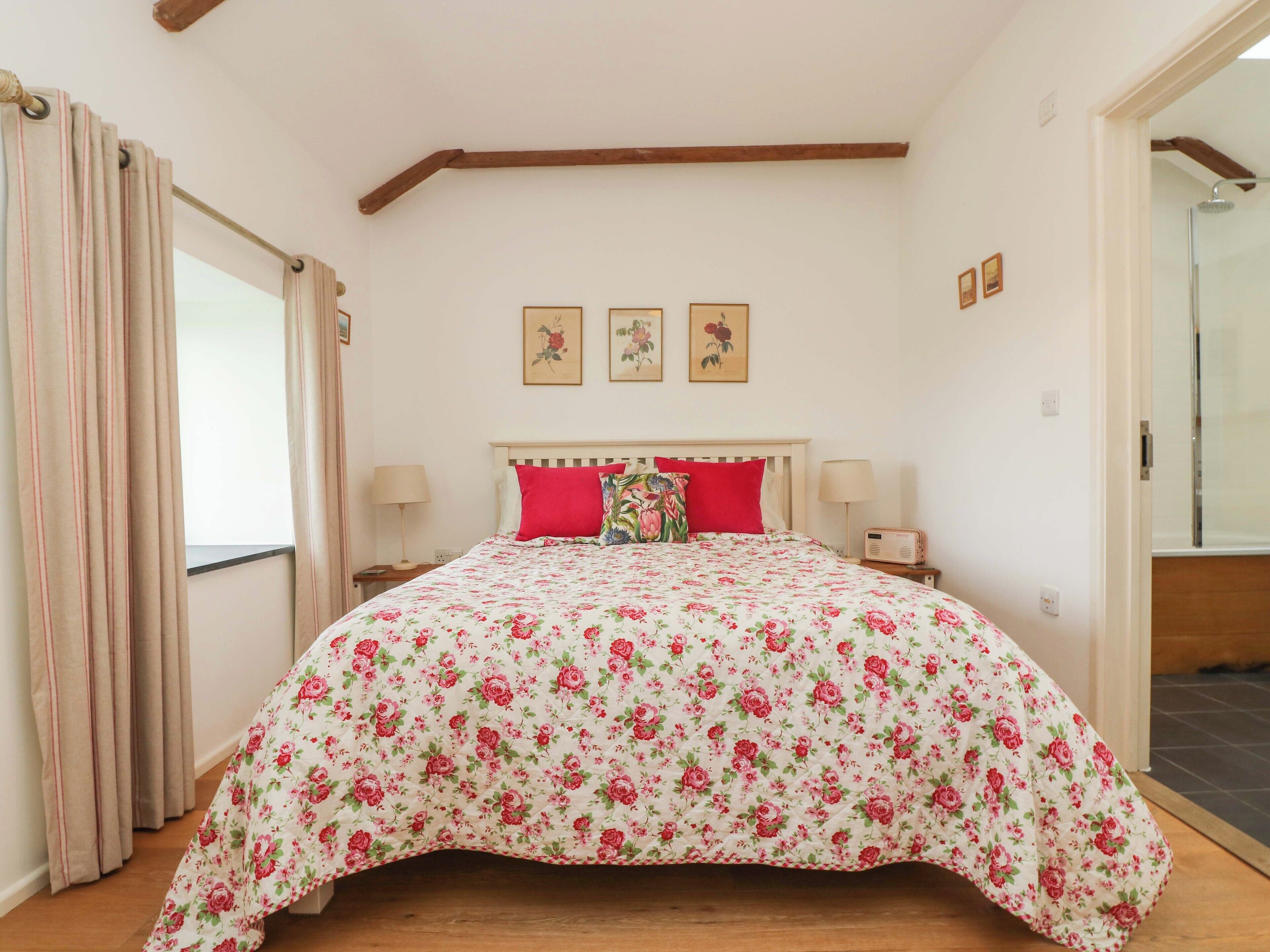 Une chambre à coucher avec une couvre-lit à motifs floraux, une tête de lit en bois, deux lampes de chevet et une fenêtre avec des rideaux.