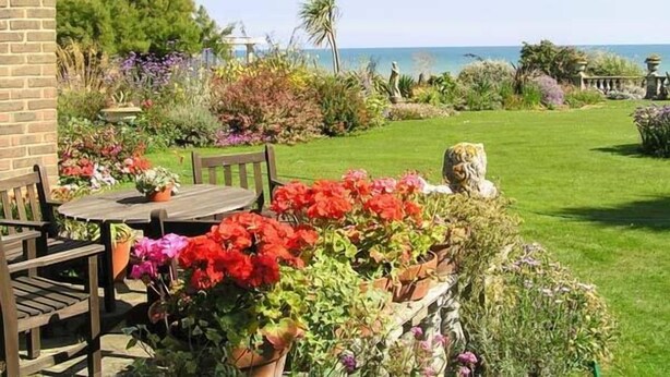 A garden with a table and chairs, a stone sculpture, and a variety of plants.