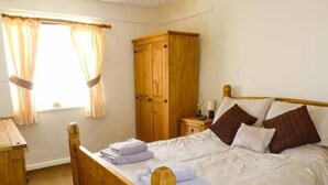 Ein Schlafzimmer mit einem hölzernen Bett, einem Nachttisch, einem Kleiderschrank und einem Fenster mit Vorhängen.