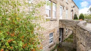 Ein Steinhaus mit einem schmalen Innenhof, einem kleinen Fenster und einer Mauer, die von Pflanzen überwuchert ist.
