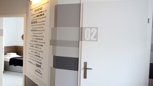 Un pasillo con una puerta blanca marcada con el número "02", un reloj en la pared y una pared con texto e imágenes.