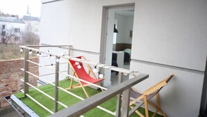 Un balcón con césped artificial, una silla roja y una silla plegable de madera.