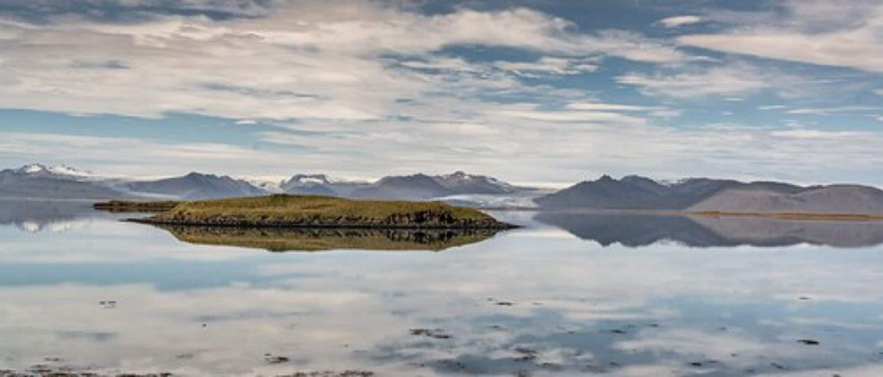 Un lago tranquilo con una pequeña isla en el centro, rodeado de montañas.