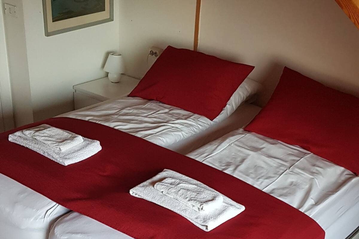 A double bed with red and white bedding, a wooden ceiling, and a framed picture on the wall.