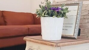 Een wit, versierd bijzettafeltje met een potplant voor een bakstenen muur en een ingelijst certificaat op een houten vloer.