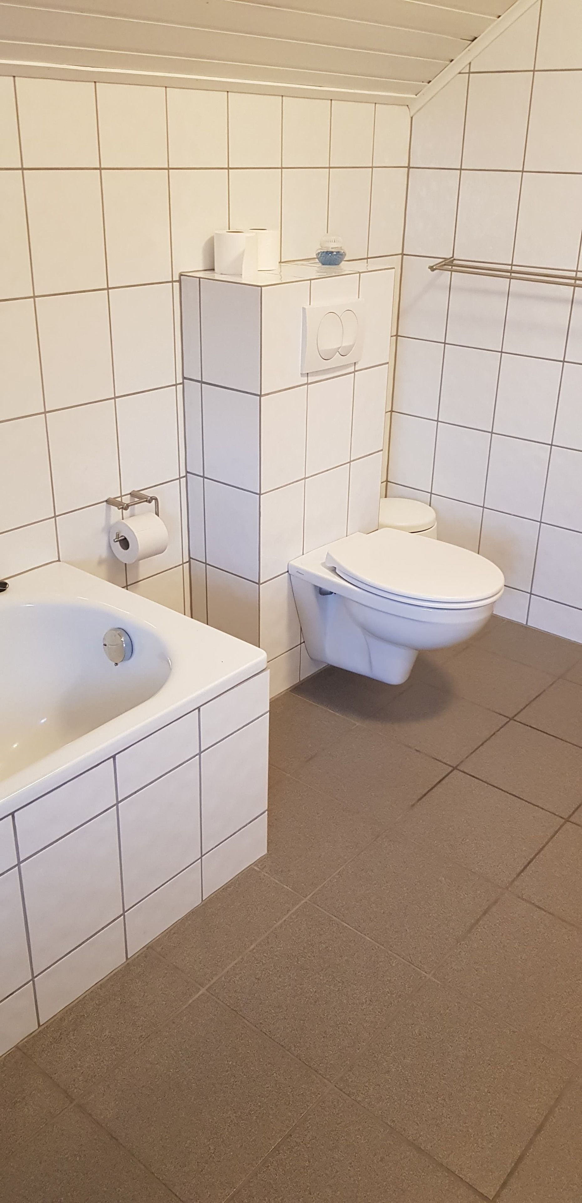 Um banheiro com azulejos brancos, uma banheira, um vaso sanitário e um porta-toalhas.