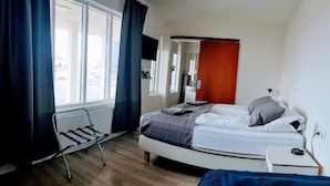 Een slaapkamer met een bed, een radiator, een raam met gordijnen en uitzicht op buiten.