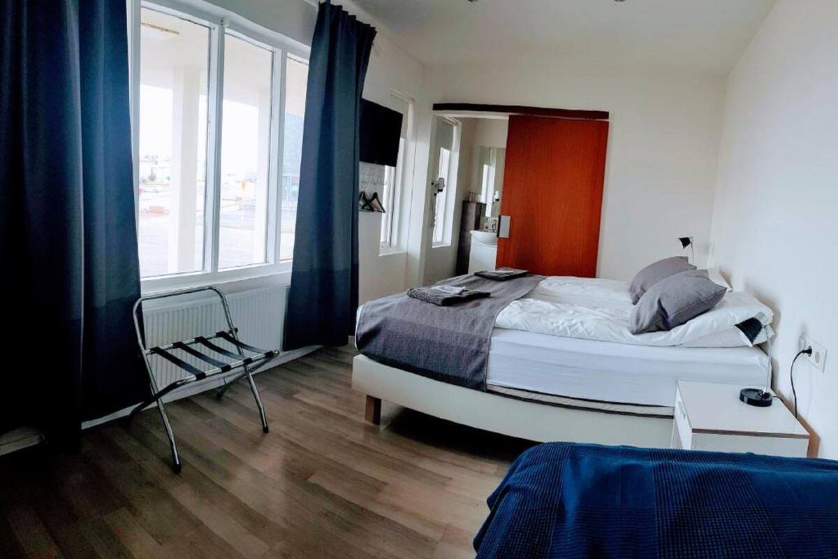 A bedroom with a bed, a radiator, a window with curtains, and a view of the outside.