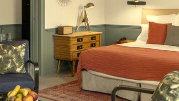 A hotel room with a bed, a desk with a bowl of fruit, a chair, a dresser, and a wall-mounted lamp.