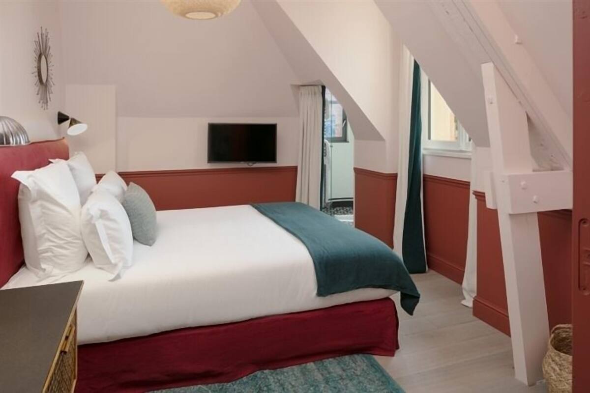 A hotel room with a bed, a television, and a view of the outside.