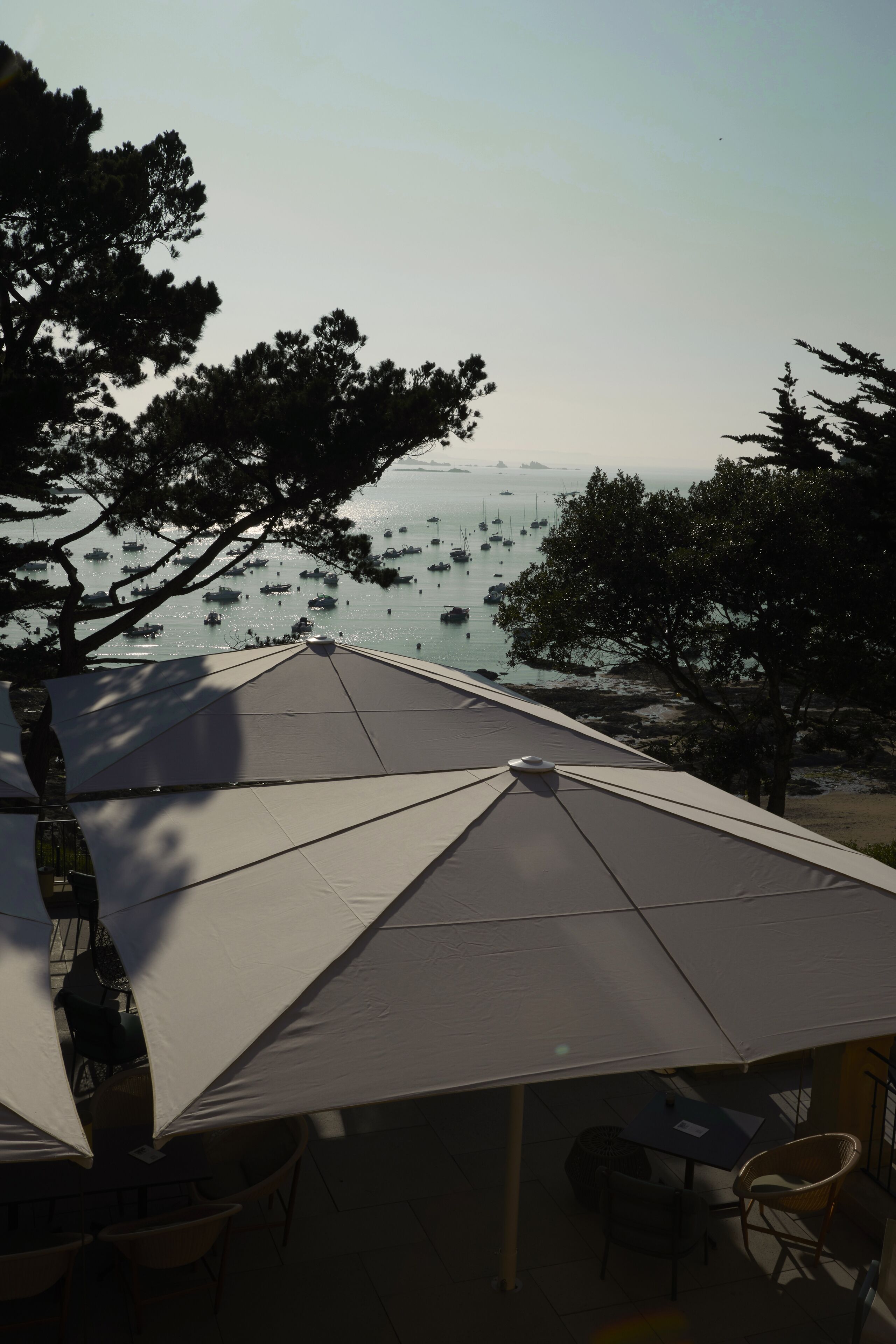 A beachside terrace with umbrellas and chairs, overlooking a calm sea with boats.