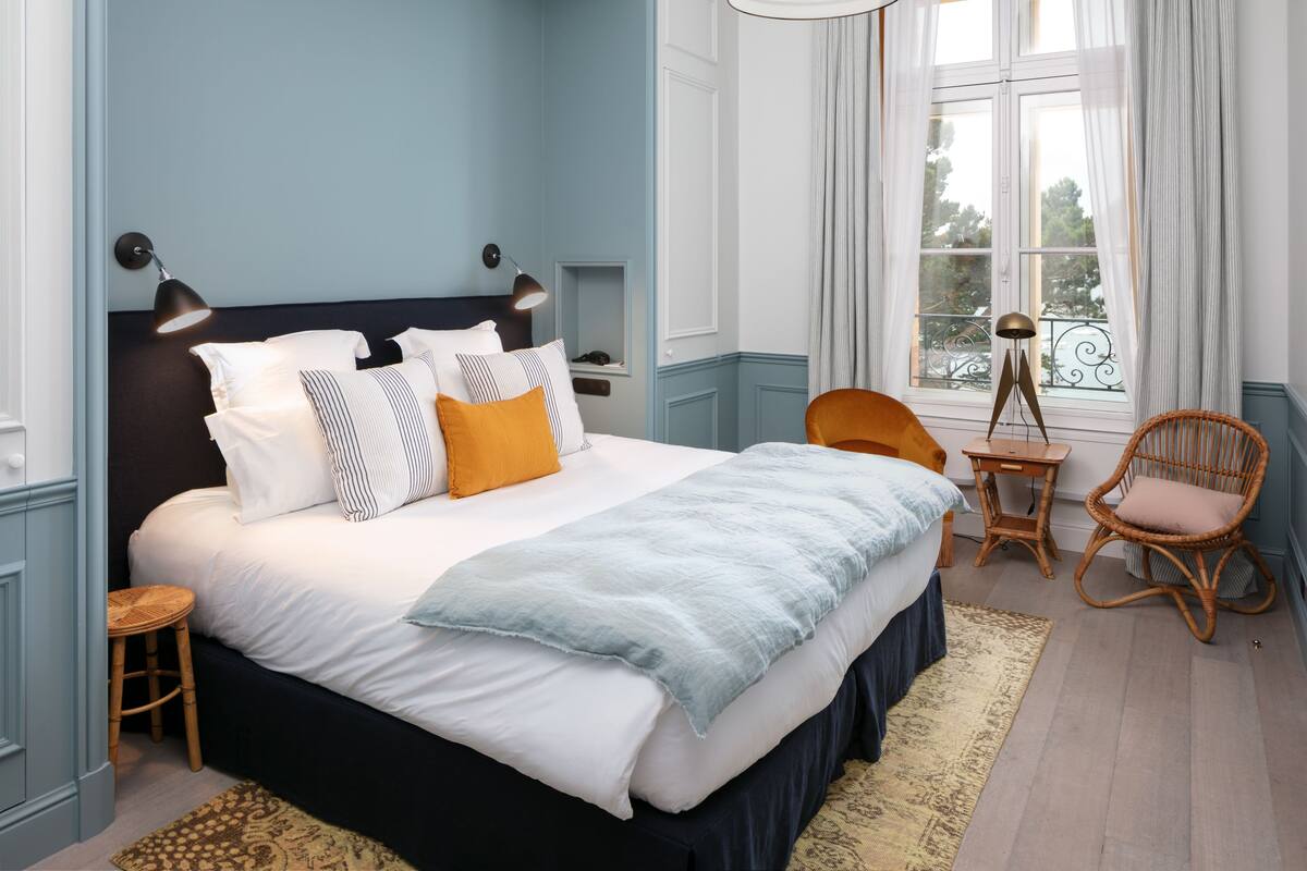 A bedroom with a bed, bedside tables, a chair, a window with curtains, and a view of the outdoors.