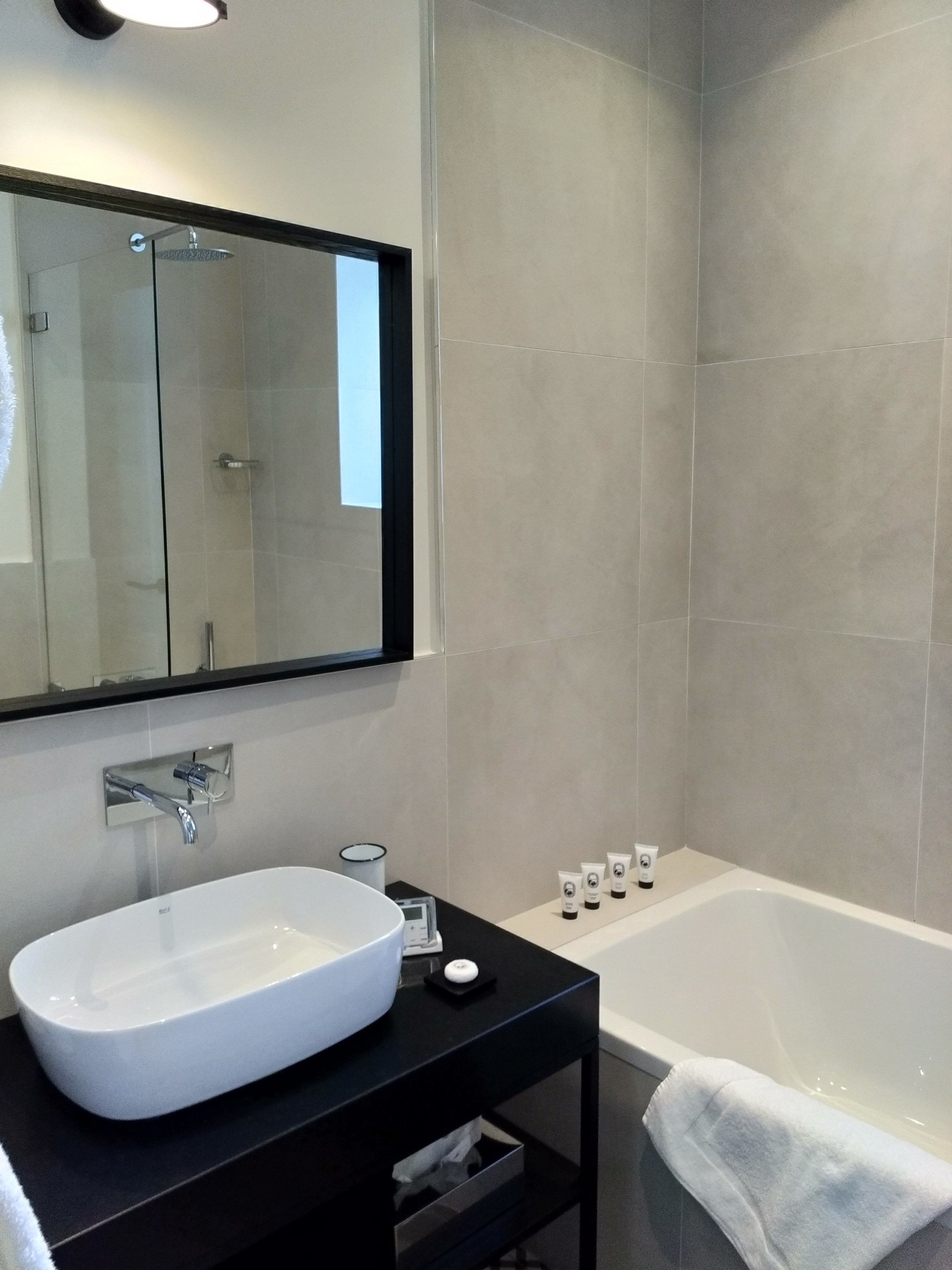 Un baño moderno con un lavabo blanco, un espejo grande, una bañera y una zona de ducha.