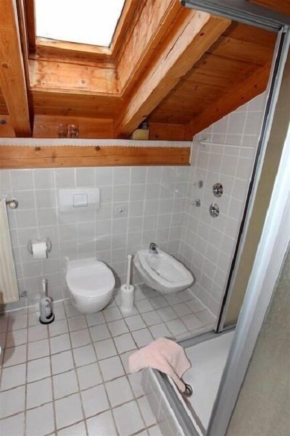 Un baño pequeño y funcional con tragaluz, inodoro, bidé y zona de ducha.