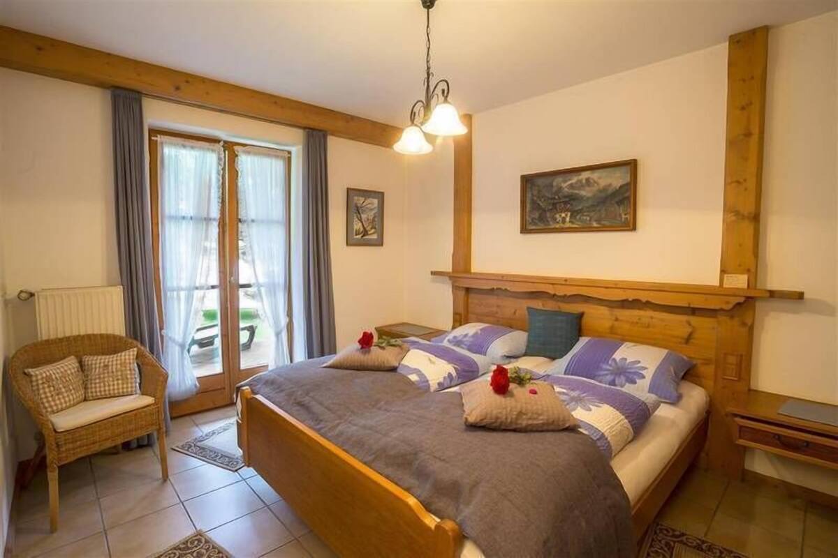 Une chambre à coucher avec un lit en bois, deux oreillers, une table de chevet, une chaise et un tableau accroché au mur.
