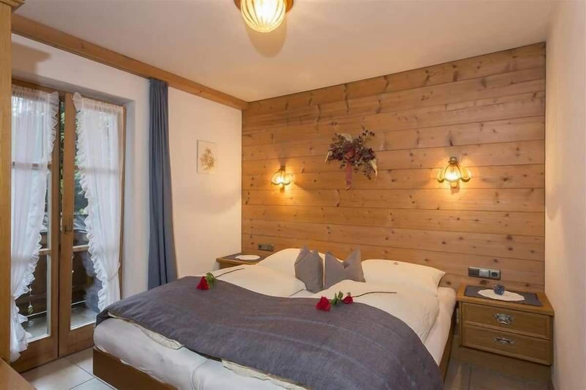 Une chambre à coucher avec une tête de lit en bois, deux lampes de chevet, un lit recouvert d’une couverture grise et une table de chevet avec une horloge.