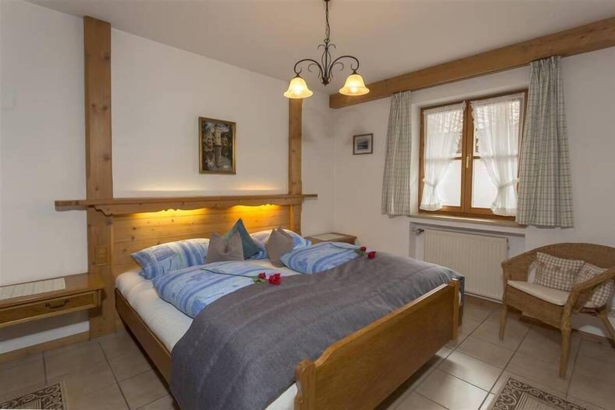 Une chambre à coucher avec un lit en bois, une table de chevet, une chaise, une fenêtre avec des rideaux et un lustre.
