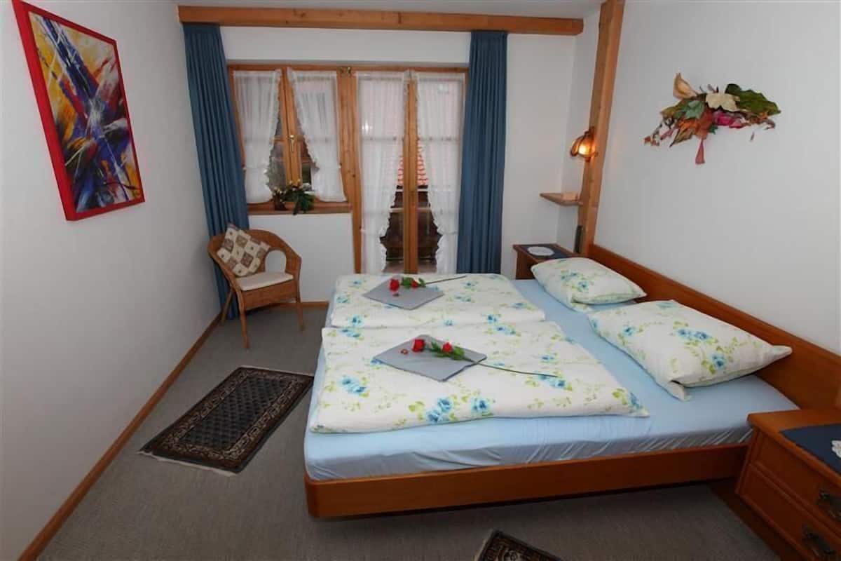 Une chambre avec deux lits, une chaise, une fenêtre avec des rideaux, un élément décoratif mural et un tapis.
