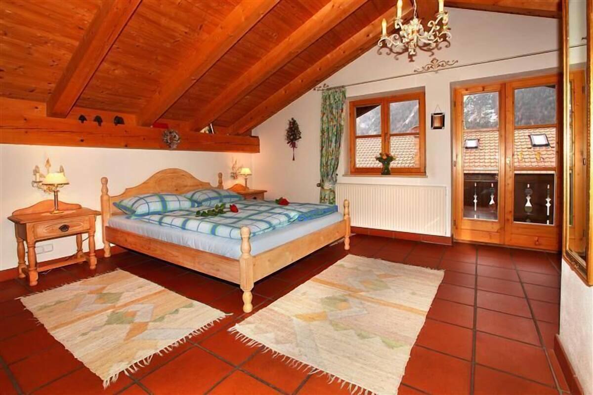 Une chambre à coucher avec un lit en bois, deux tables de chevet, un lustre, une fenêtre avec des volets et un radiateur.