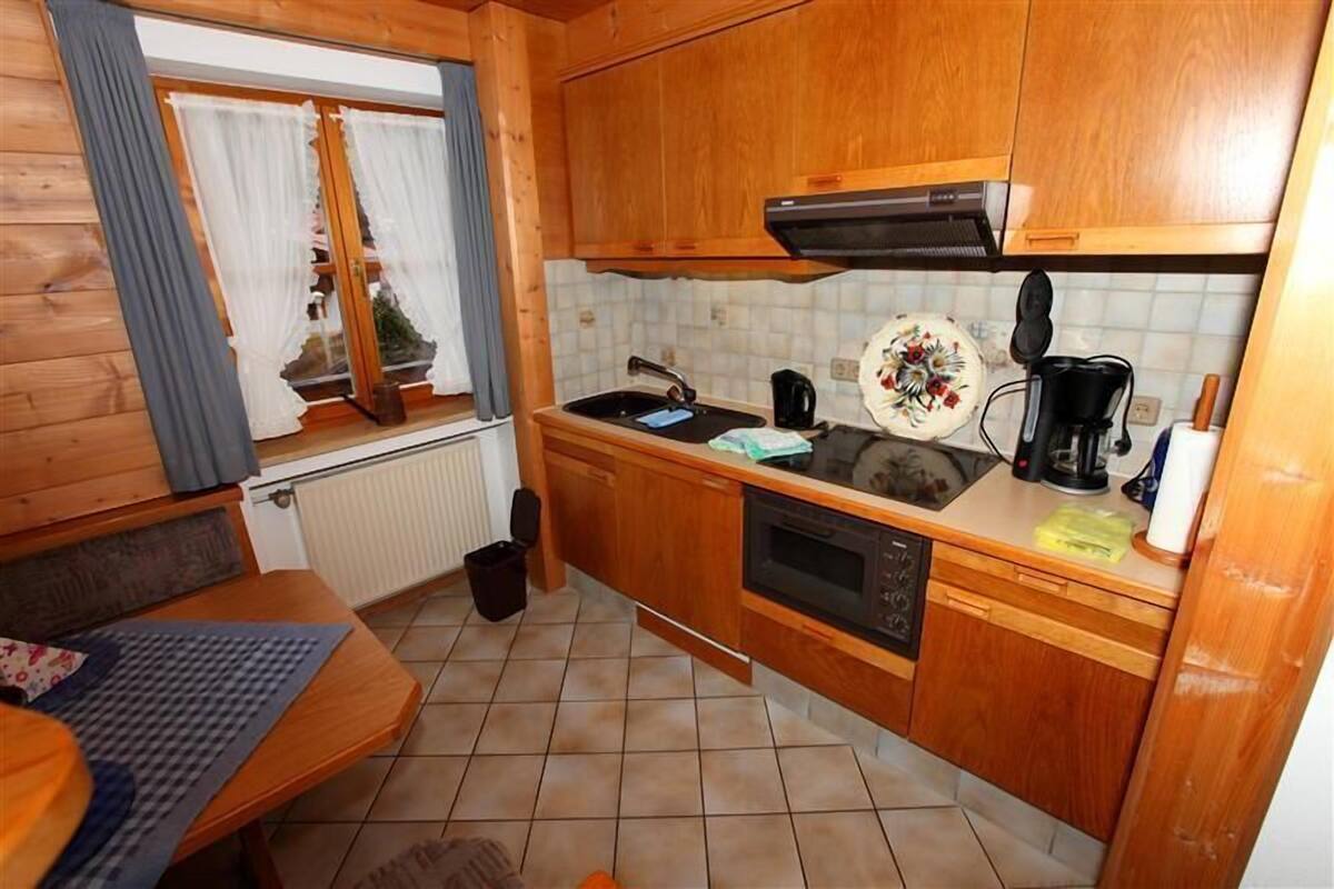 Une cuisine compacte avec des meubles en bois, un four encastré, un évier et une fenêtre avec des rideaux.