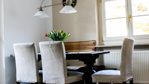 A dining area with a table and four chairs, a clock on the wall, and a window with a view. - Alpenlodge (Garmisch-Partenkirchen)