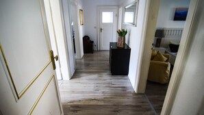 A hallway with wooden flooring, a black desk with a vase of flowers, and a yellow armchair. - Alpenlodge (Garmisch-Partenkirchen)