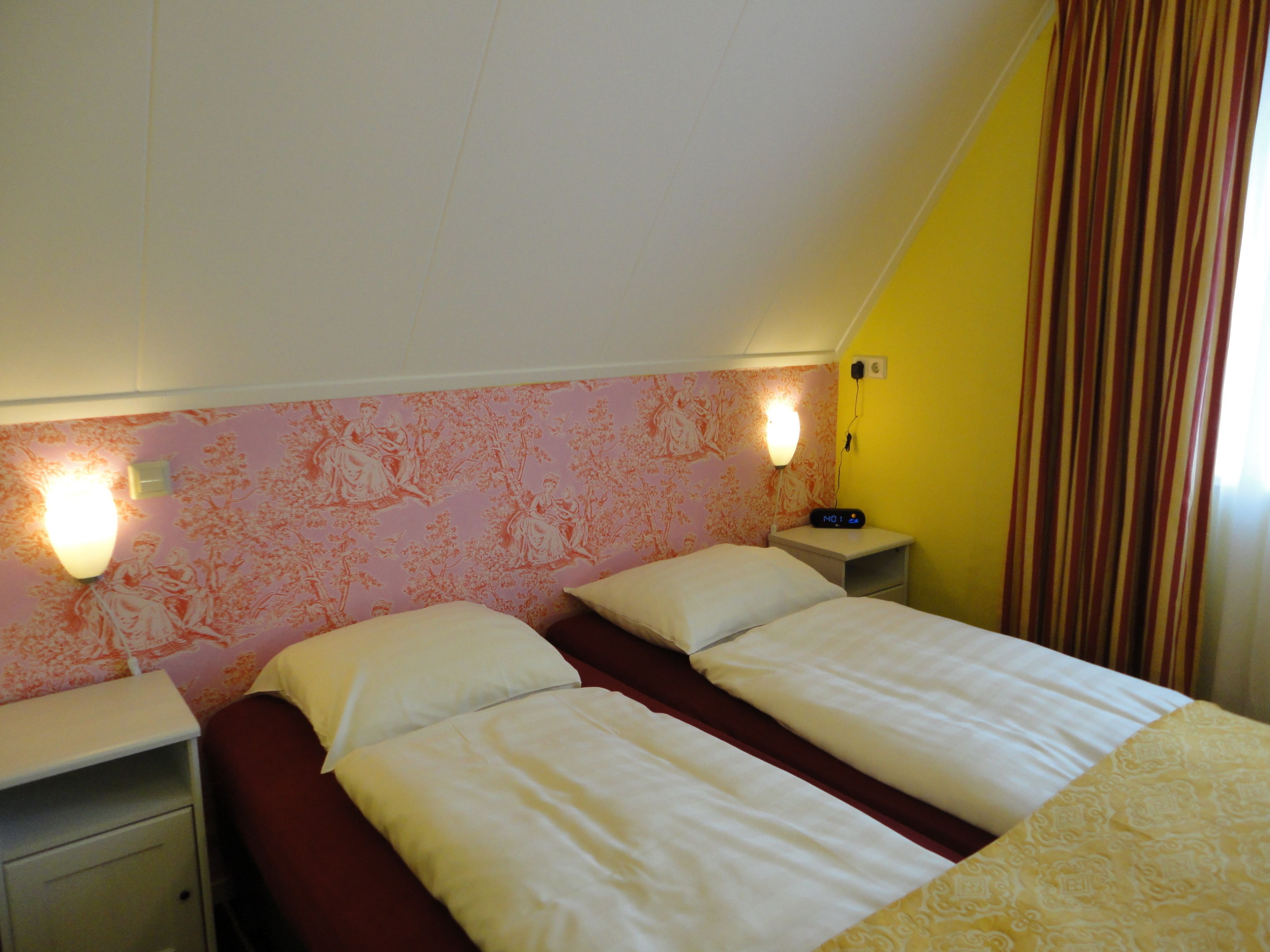 A twin room with two beds, a nightstand, a wall-mounted lamp, and a clock.