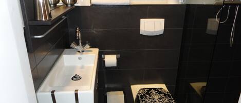 A modern bathroom with a white sink, black toilet, and a glass shower enclosure.