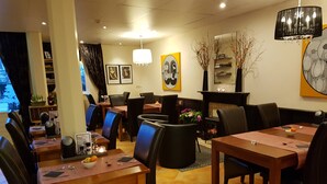 A restaurant with multiple tables and chairs, a fireplace, and artwork on the walls. - Hotel De Vier Seizoenen (Renesse)