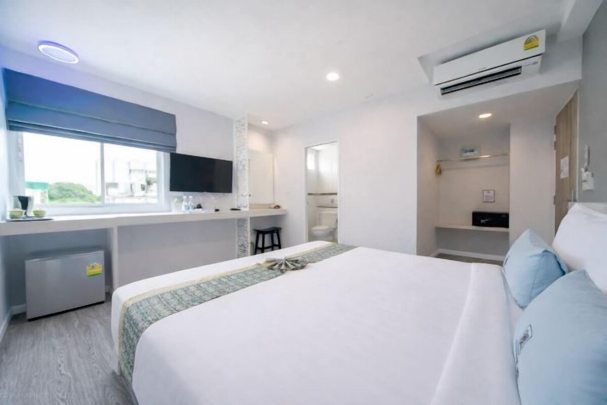 Ein modernes Hotelzimmer mit einem großen Bett, einem kleinen Schreibtisch, einem Fernseher und einem Fenster.