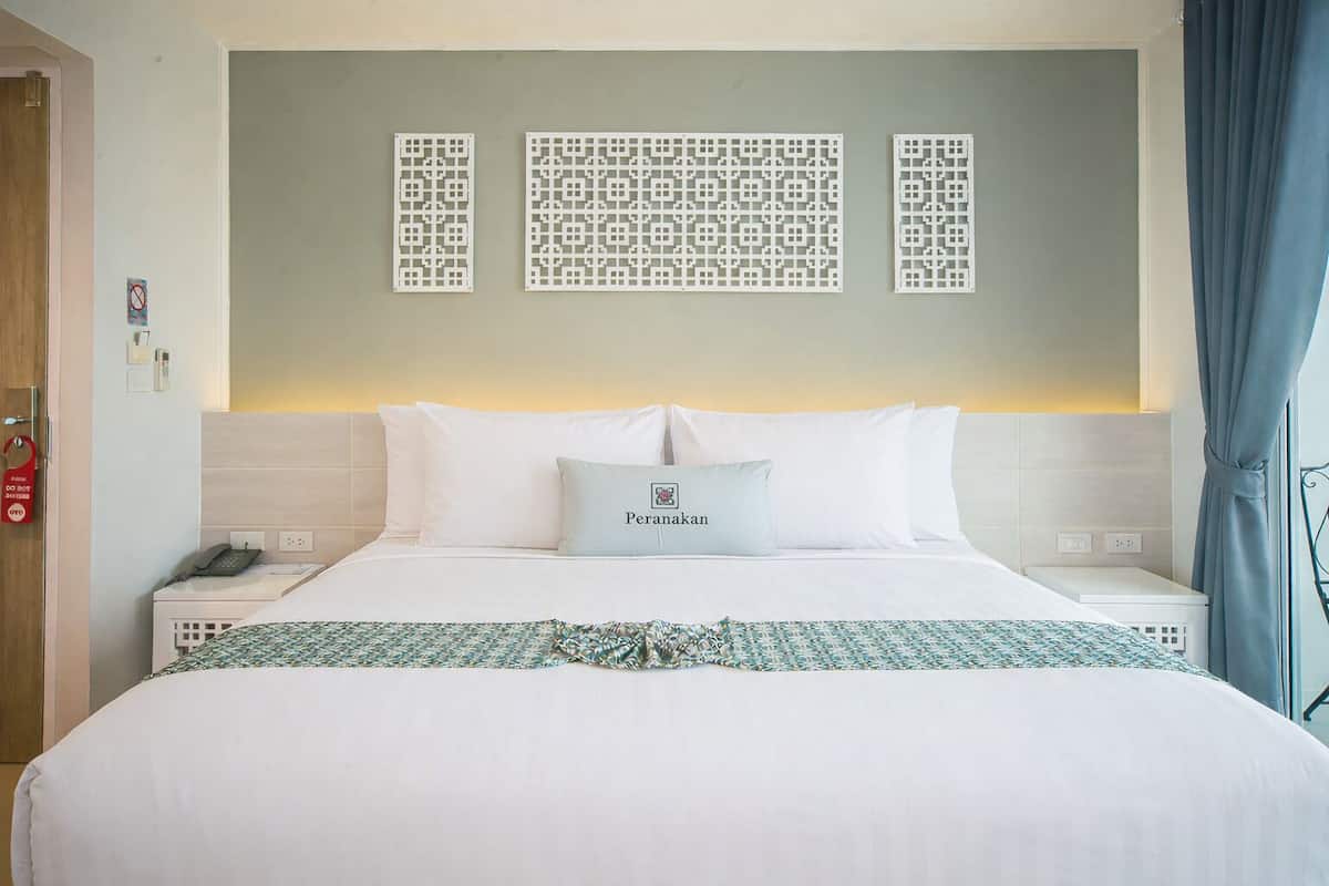 Une chambre d’hôtel avec un grand lit, un téléphone sur la table de chevet, un panneau décoratif au mur et un oreiller avec une étiquette nominative.