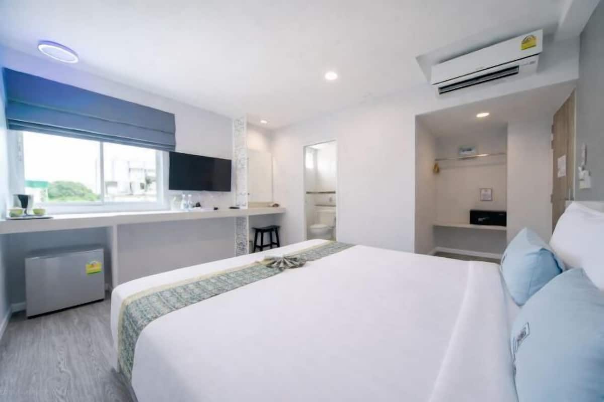 Une chambre d’hôtel moderne avec un grand lit, un petit bureau, une télévision et une fenêtre.