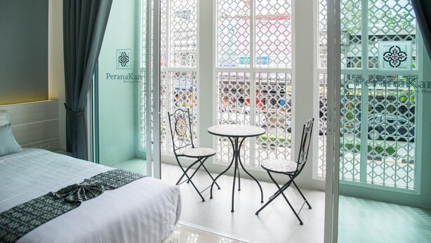 A hotel room with a bed, a small table, two chairs, and a balcony with a view of the street. - Peranakan Boutique Hotel (Phuket)