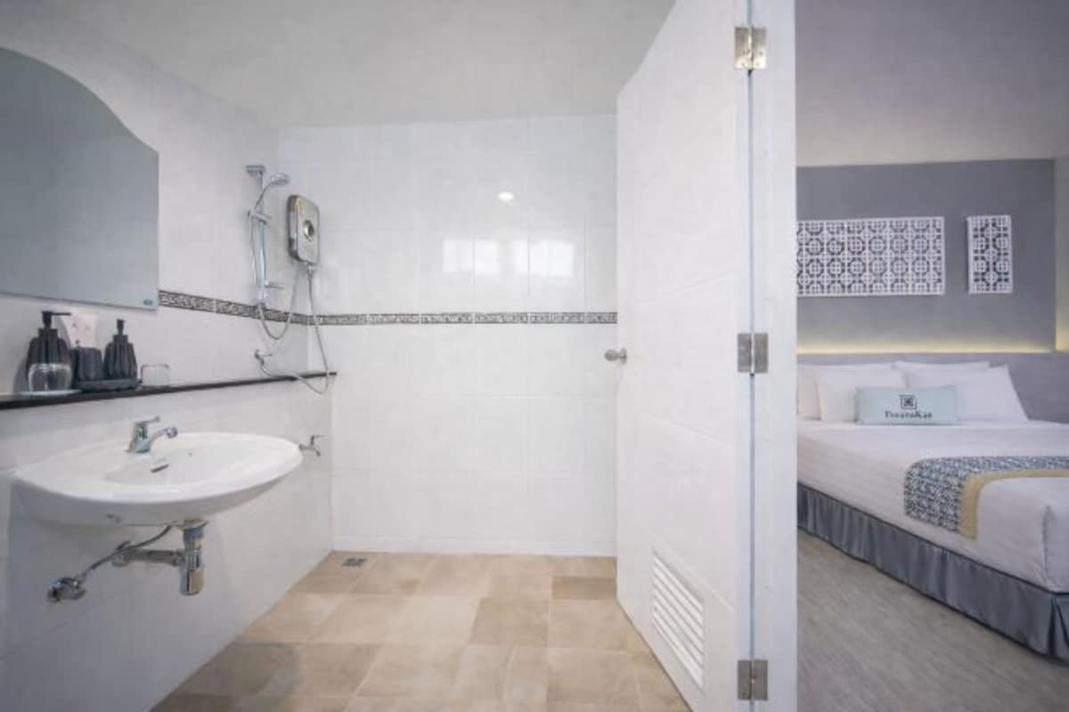 Un baño con lavamanos, ducha y una cama frente a una pared con diseño.