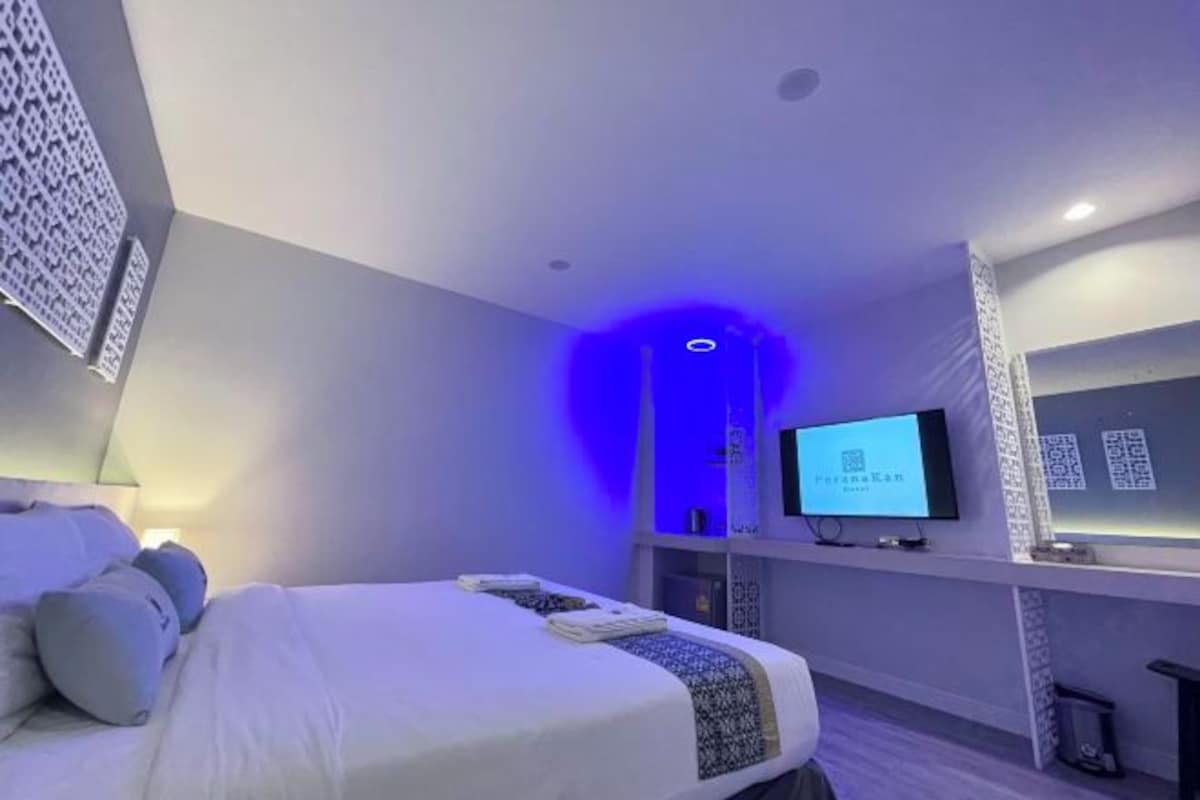 Una habitación de hotel moderna con una cama bien hecha, un televisor de pantalla plana montado en la pared y una luz ambiental azul.