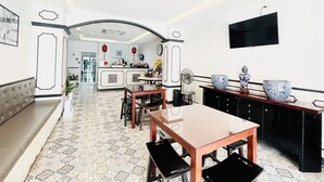 A spacious living area with a dining table and chairs, a sofa, a TV mounted on the wall, and a kitchen area in the background. - Peranakan Boutique Hotel (Phuket)